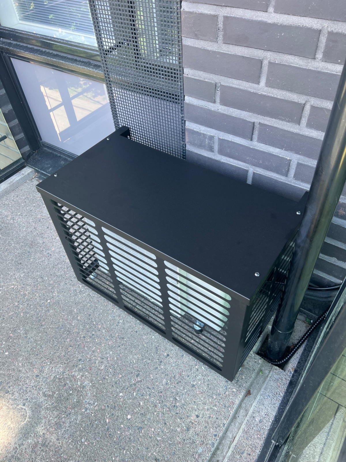 Black metal heat pump outdoor-unit cover beside a grey brick wall