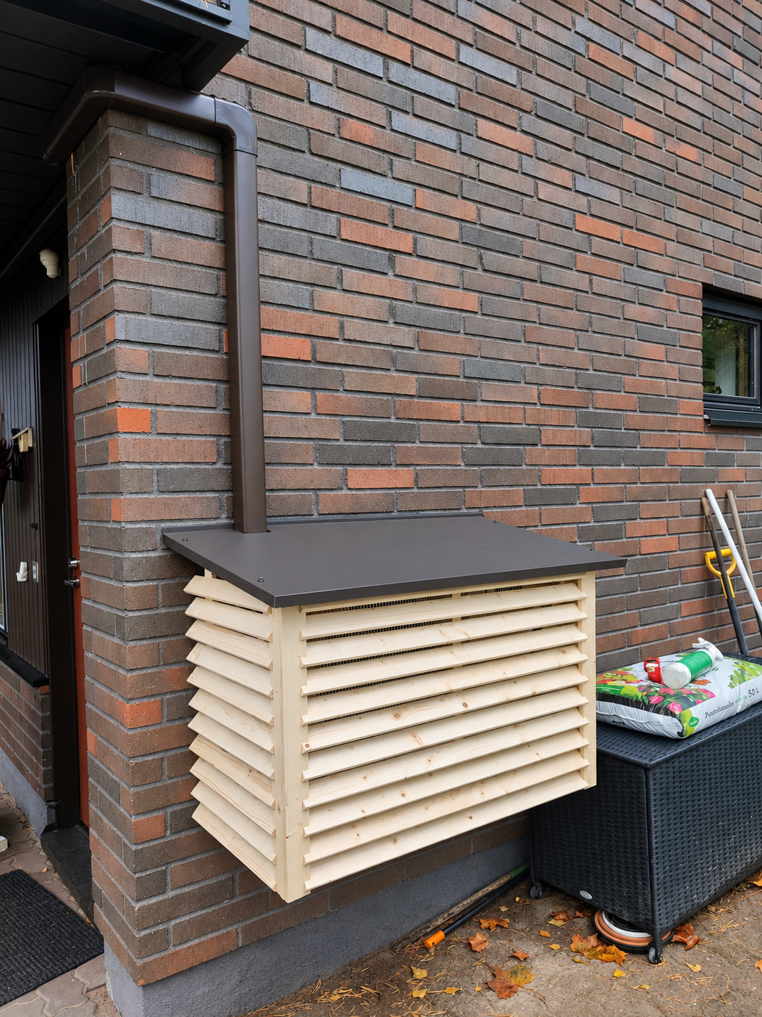 Brown pipe trunking and a wooden outdoor-unit cover on a brick facade