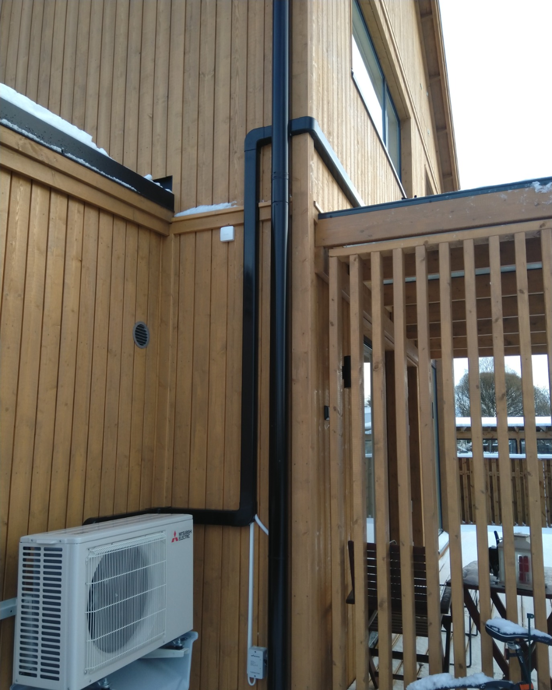 Heat pump outdoor unit and dark pipe trunking on a timber-clad house